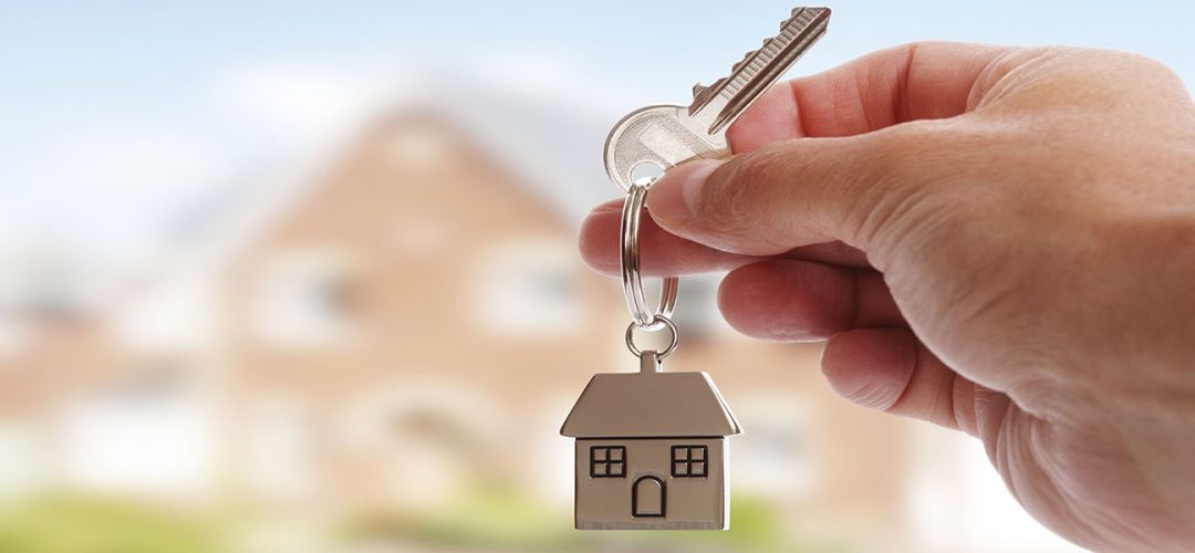 Holding house keys on house shaped keychain in front of a new home